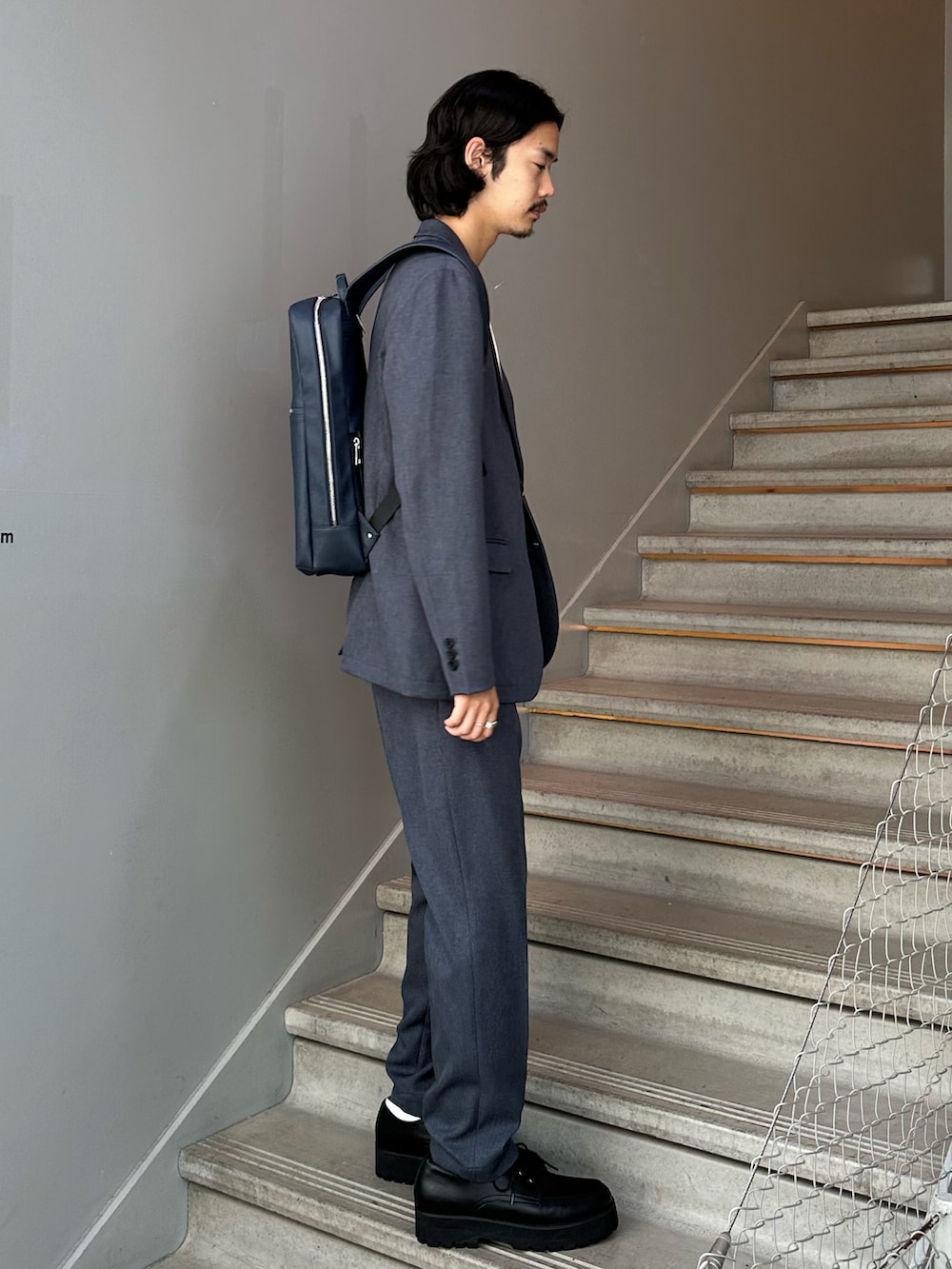 グレー系のセットアップ、ブルー系のバックパック/リュック、ブラック系のその他シューズを着用したメンズの夏コーディネートの3枚目の写真