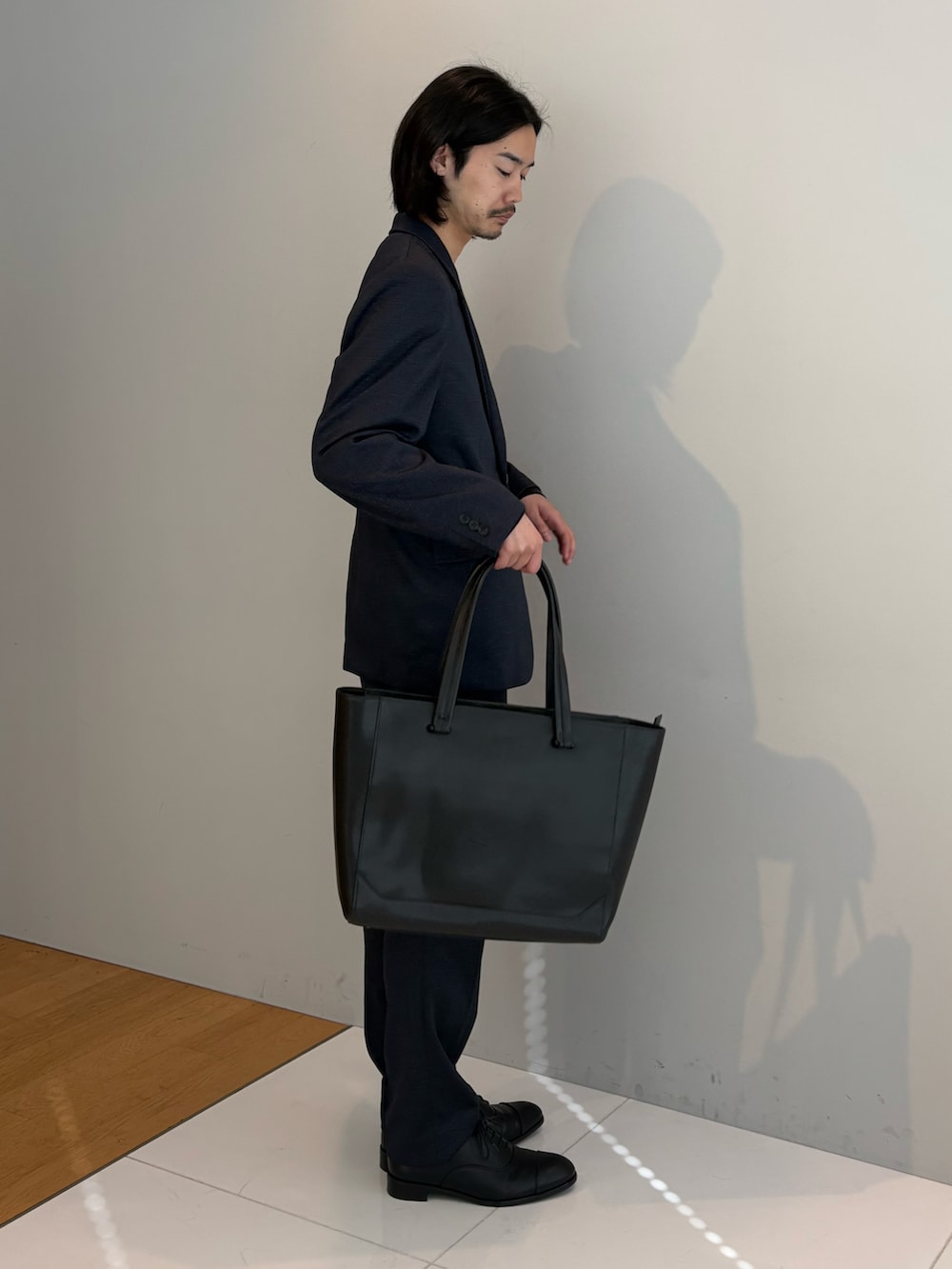 ブラック系のトートバッグ、ブルー系のセットアップ、ブラック系のドレスシューズを着用したメンズの冬コーディネートの2枚目の写真