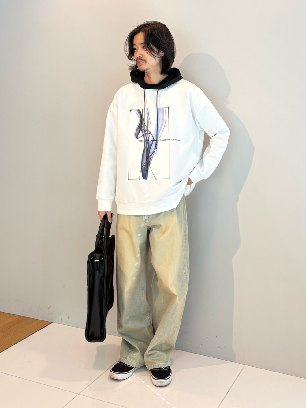 ブラック系のトートバッグ、ホワイト系のパーカー、ブルー系のデニムパンツを着用したメンズの冬コーディネートの2枚目の写真