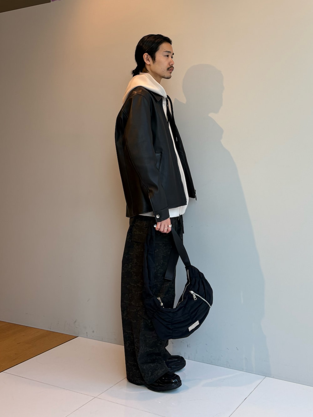 ブラック系のブルゾン、ベージュ系のパーカー、ブラック系のショルダーバッグを着用したメンズの春コーディネートの2枚目の写真