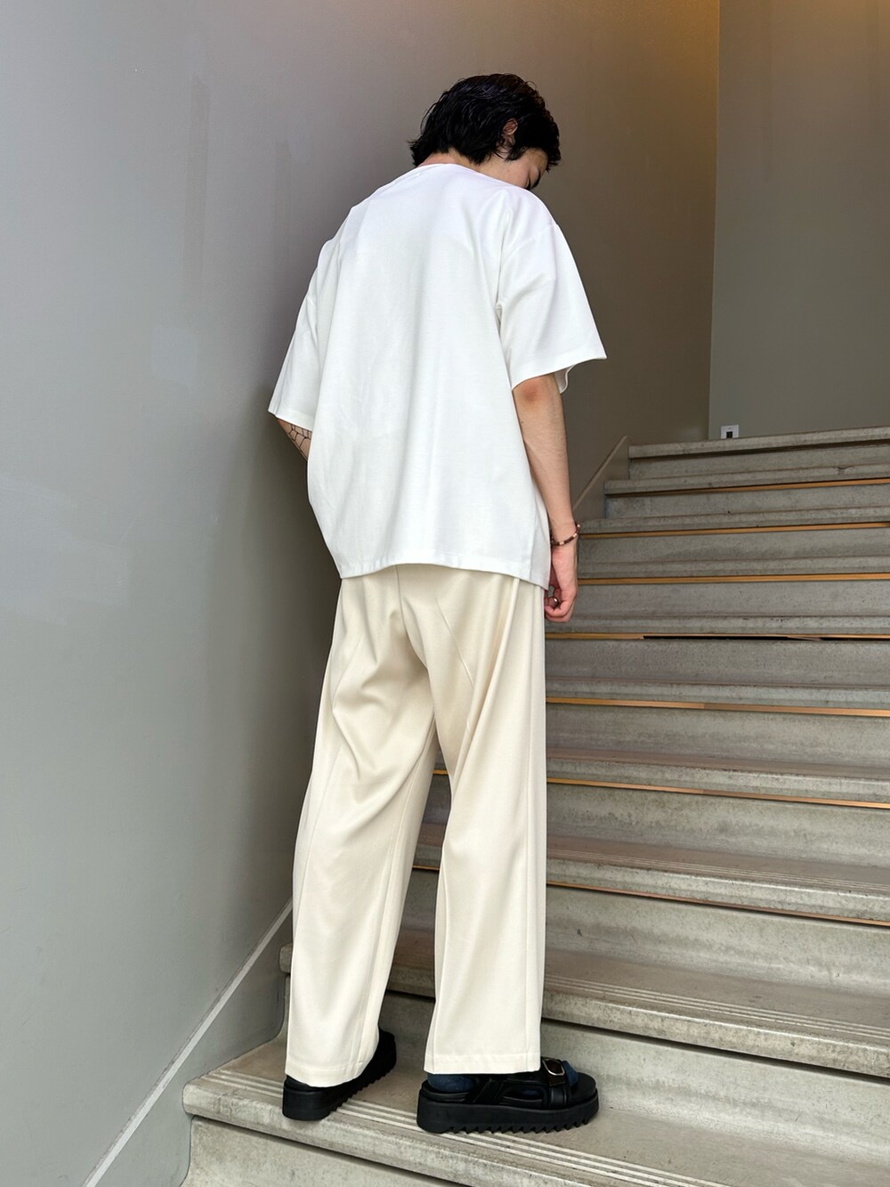 ホワイト系のTシャツ/カットソー、ホワイト系のスラックス、ブラック系のサンダルを着用したメンズの夏コーディネートの2枚目の写真