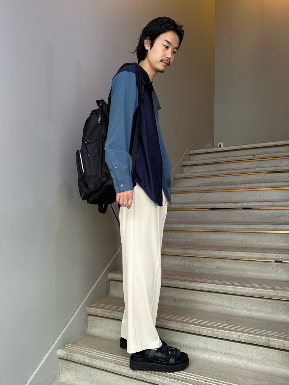 ブラック系のバックパック/リュック、ブラック系のサンダル、ホワイト系のスラックスを着用したメンズの夏コーディネートの3枚目の写真