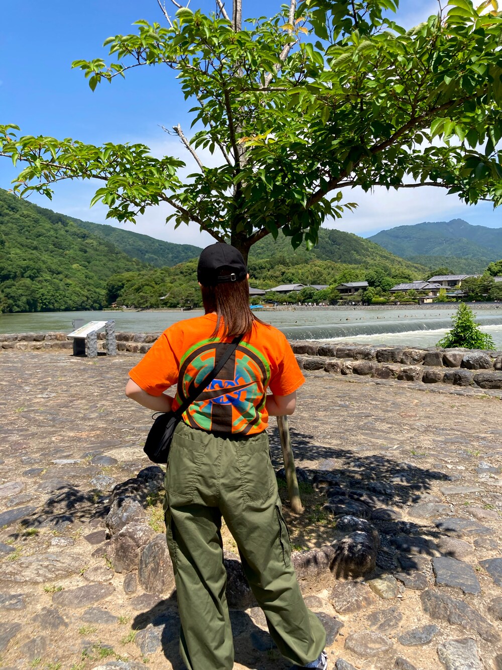 グリーン系のカーゴパンツ、ブラック系のスニーカー、オレンジ系のTシャツ/カットソーを着用したレディースの夏コーディネートの2枚目の写真