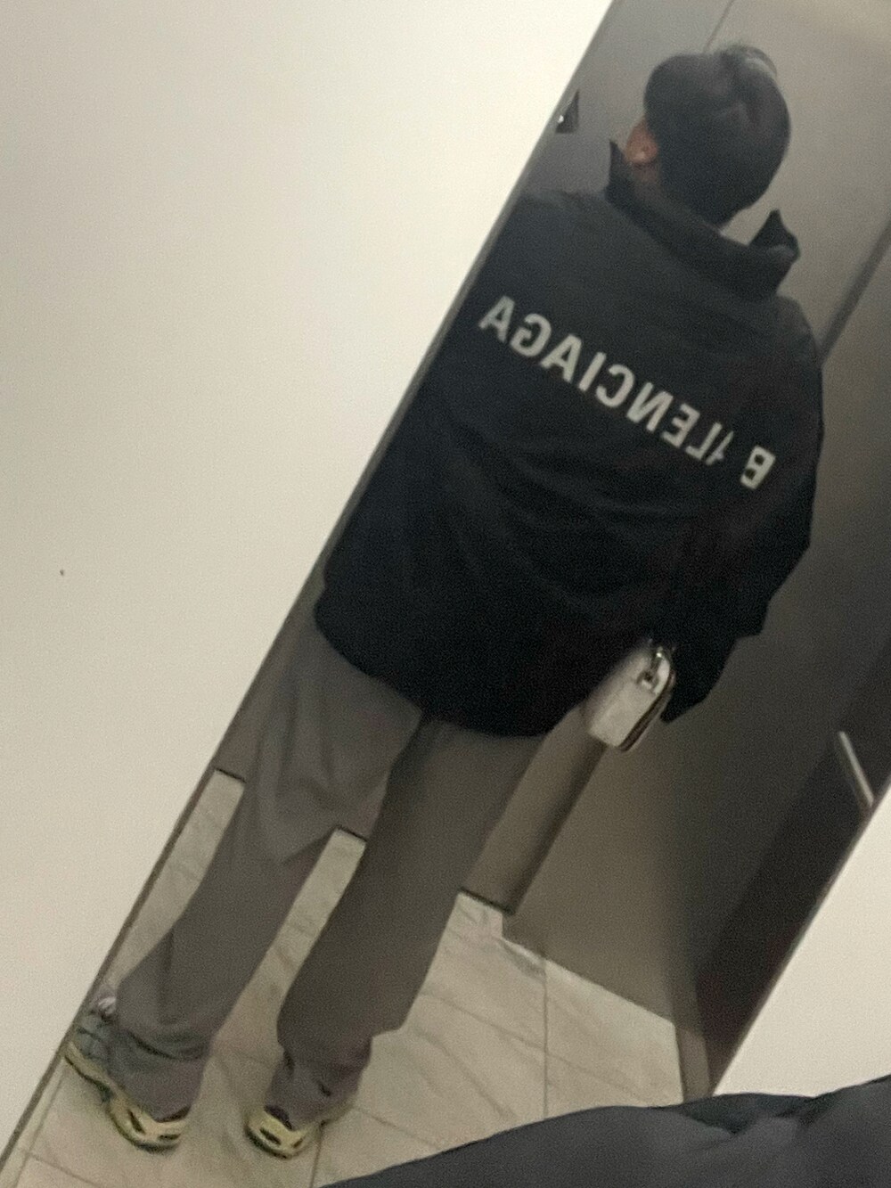 グレー系のスラックス、ブラック系のダウンジャケット/コート、ホワイト系のメッセンジャーバッグを着用したメンズの冬コーディネートの2枚目の写真