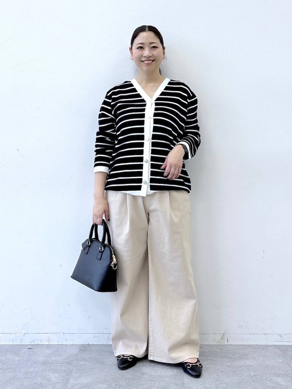 ブラック系のハンドバッグ、ベージュ系のデニムパンツ、ブラック系のカーディガン/ボレロを着用したレディースの冬コーディネートの2枚目の写真