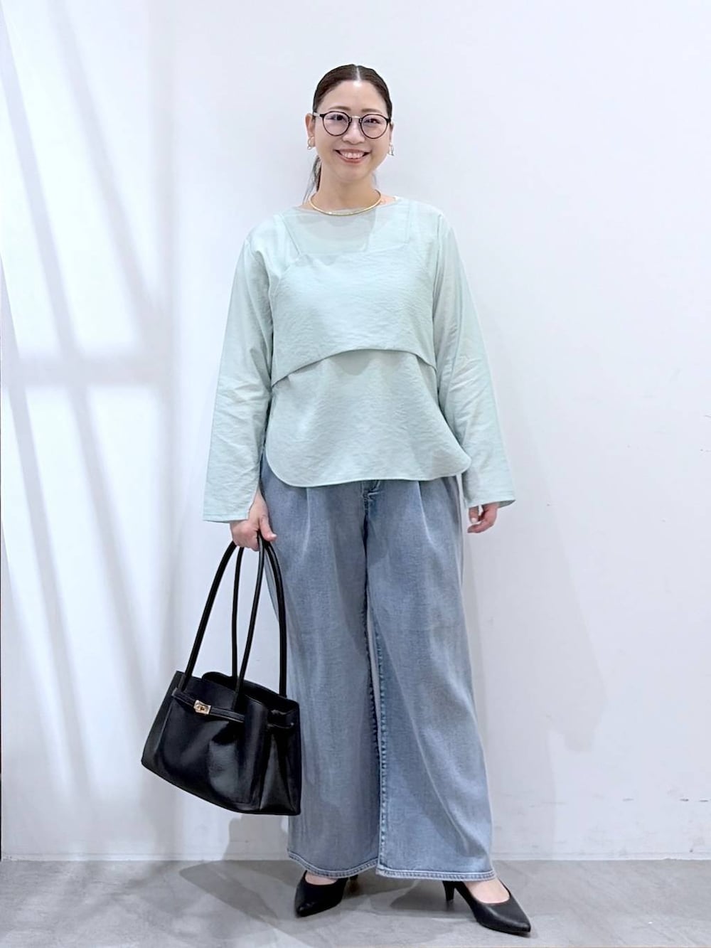 ブルー系のデニムパンツ、ブラック系のハンドバッグ、グリーン系のシャツ/ブラウスを着用したレディースの春コーディネートの2枚目の写真