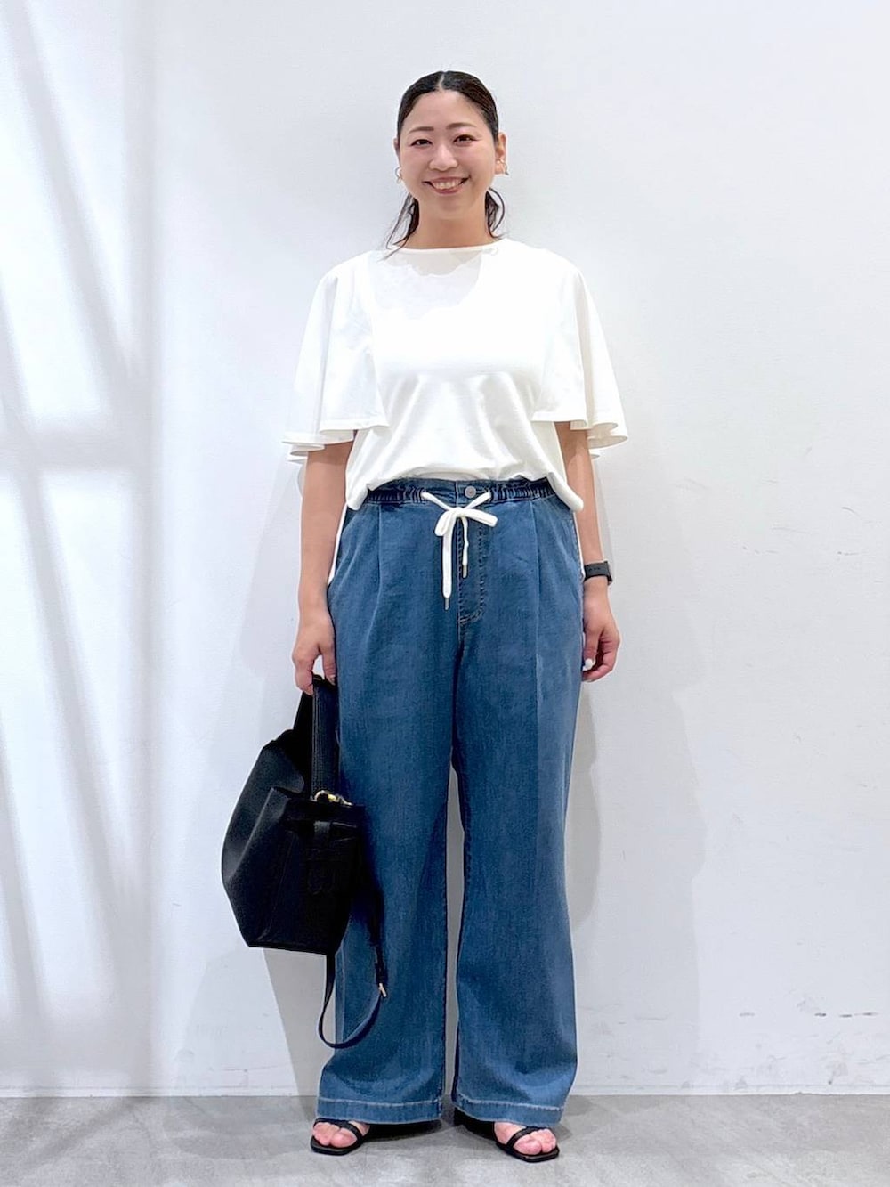 ブラック系のハンドバッグ、ブラック系のサンダル、ブルー系のデニムパンツを着用したレディースの夏コーディネートの2枚目の写真