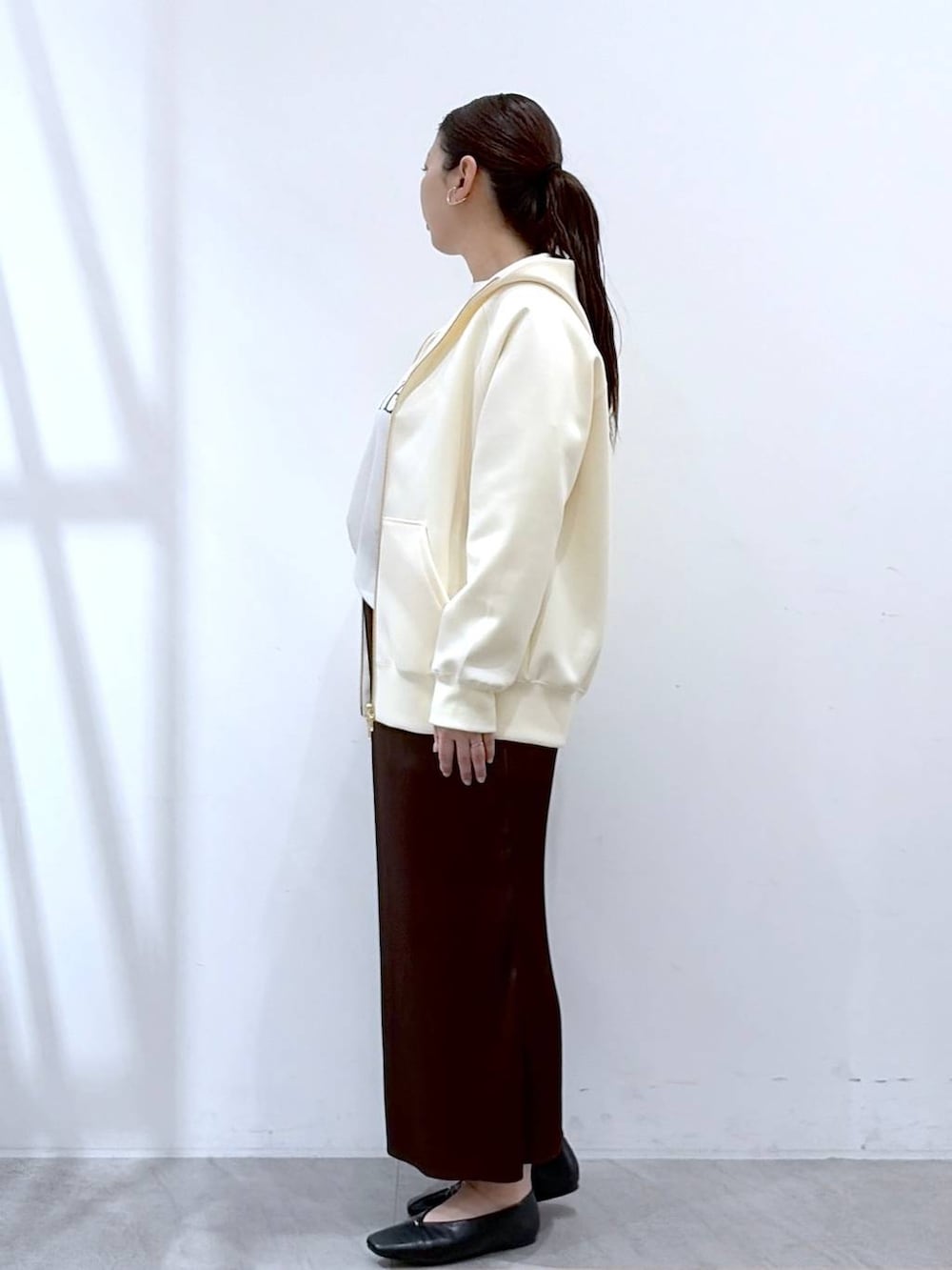 ホワイト系のパーカー、ブラウン系のスカート、ブラック系のショルダーバッグを着用したレディースの春コーディネートの3枚目の写真