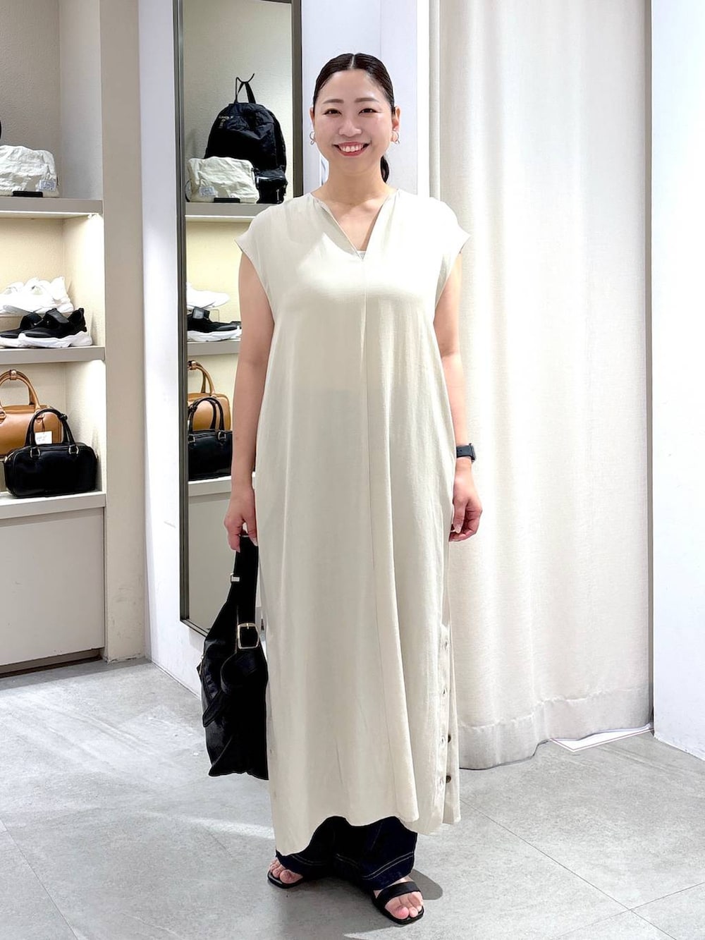 ブルー系のデニムパンツ、ブラック系のハンドバッグ、ベージュ系のワンピースを着用したレディースの春コーディネートの2枚目の写真