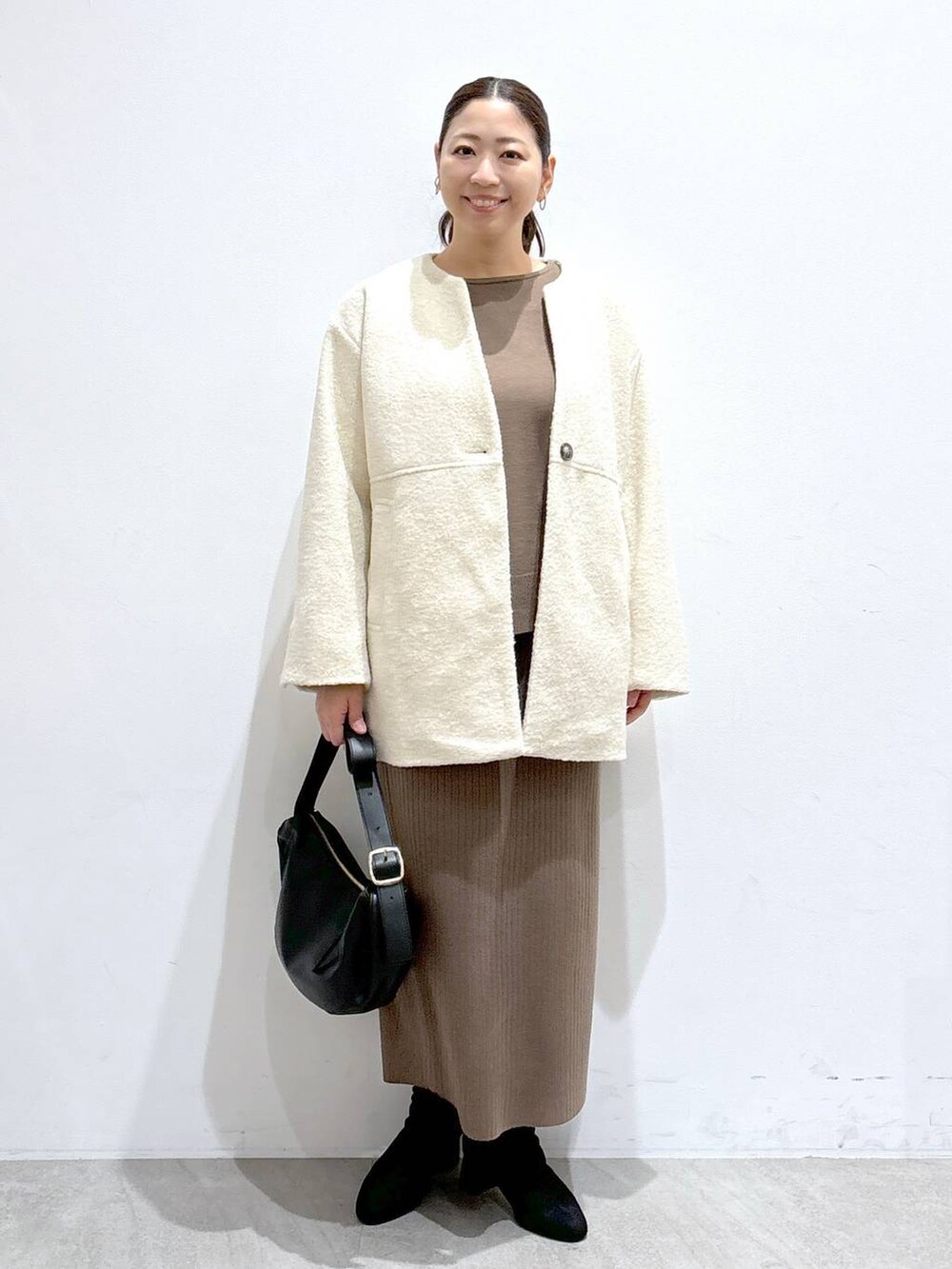 グレー系のブーツ、ブラック系のハンドバッグ、ホワイト系のその他アウターを着用したレディースの冬コーディネートの2枚目の写真