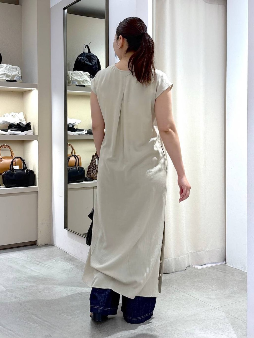 ブルー系のデニムパンツ、ブラック系のハンドバッグ、ベージュ系のワンピースを着用したレディースの春コーディネートの4枚目の写真