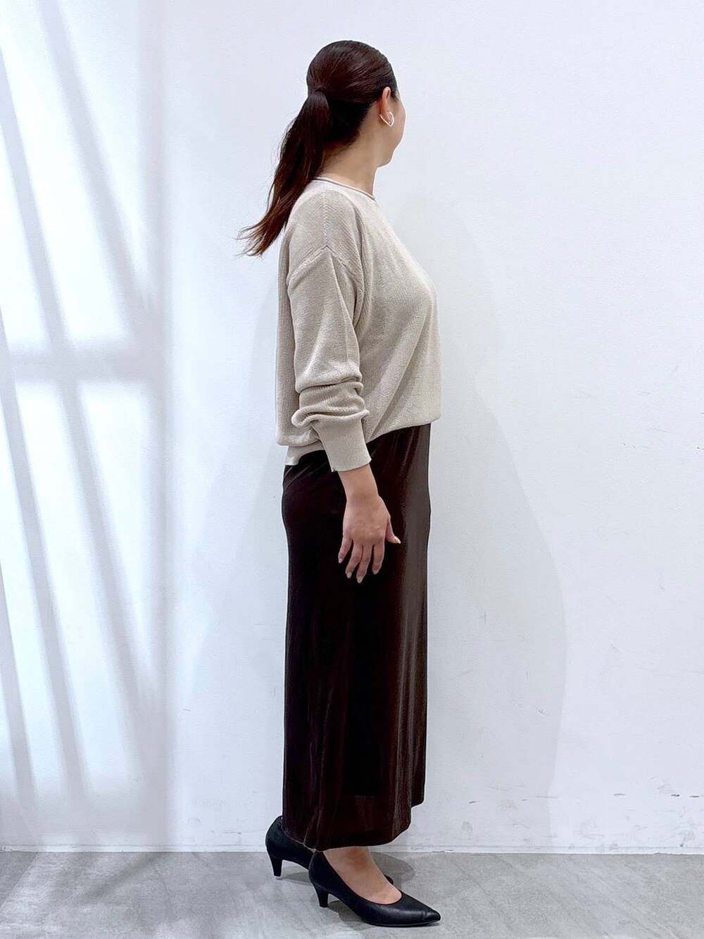 ブラック系のパンプス、ブラック系のハンドバッグ、ブラウン系のスカートを着用したレディースの秋コーディネートの5枚目の写真