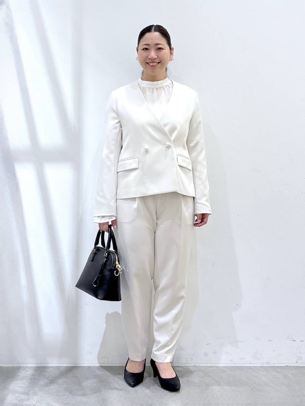 ブラック系のハンドバッグ、ホワイト系のシャツ/ブラウス、ホワイト系のノーカラージャケットを着用したレディースの春コーディネートの2枚目の写真