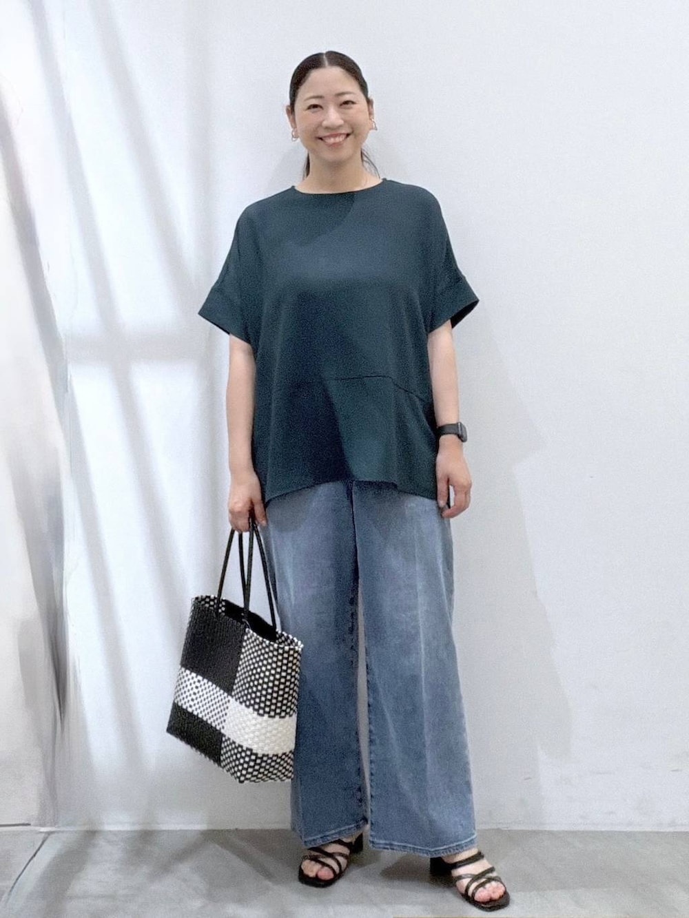 ブラック系のサンダル、ホワイト系のかごバッグ、ブルー系のデニムパンツを着用したレディースの夏コーディネートの2枚目の写真