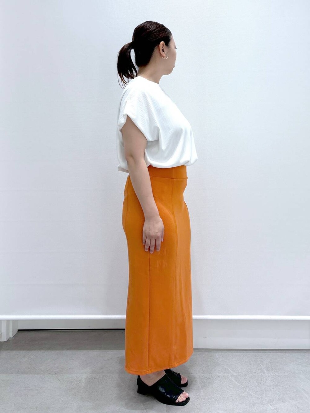 ブラック系のサンダル、ホワイト系のTシャツ/カットソー、オレンジ系のスカートを着用したレディースの春コーディネートの5枚目の写真