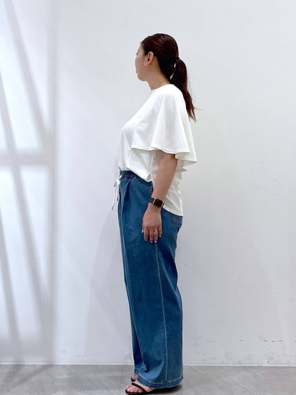 ブラック系のハンドバッグ、ブラック系のサンダル、ブルー系のデニムパンツを着用したレディースの夏コーディネートの3枚目の写真