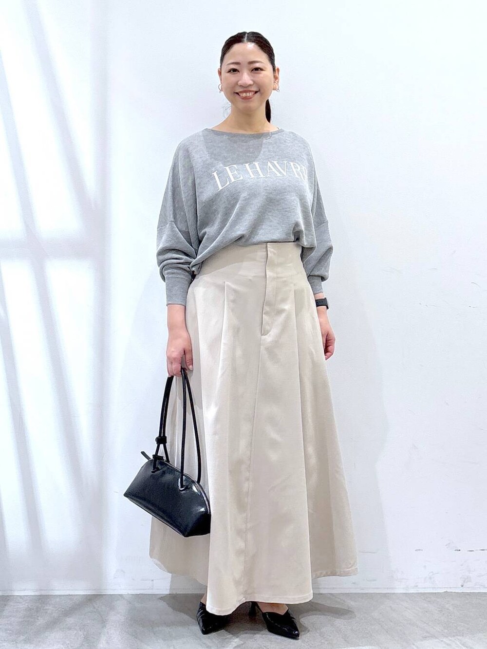 ブラック系のハンドバッグ、グレー系のニット/セーター、ベージュ系のスカートを着用したレディースの春コーディネートの2枚目の写真