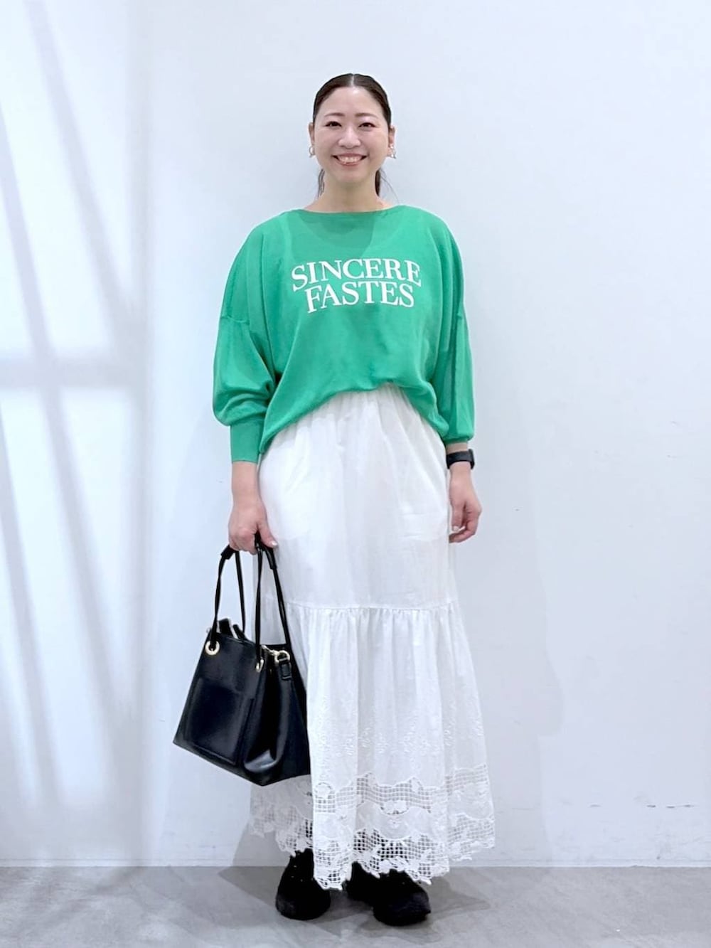 ブラック系のトートバッグ、ホワイト系のスカート、グリーン系のカーディガン/ボレロを着用したレディースの春コーディネートの2枚目の写真