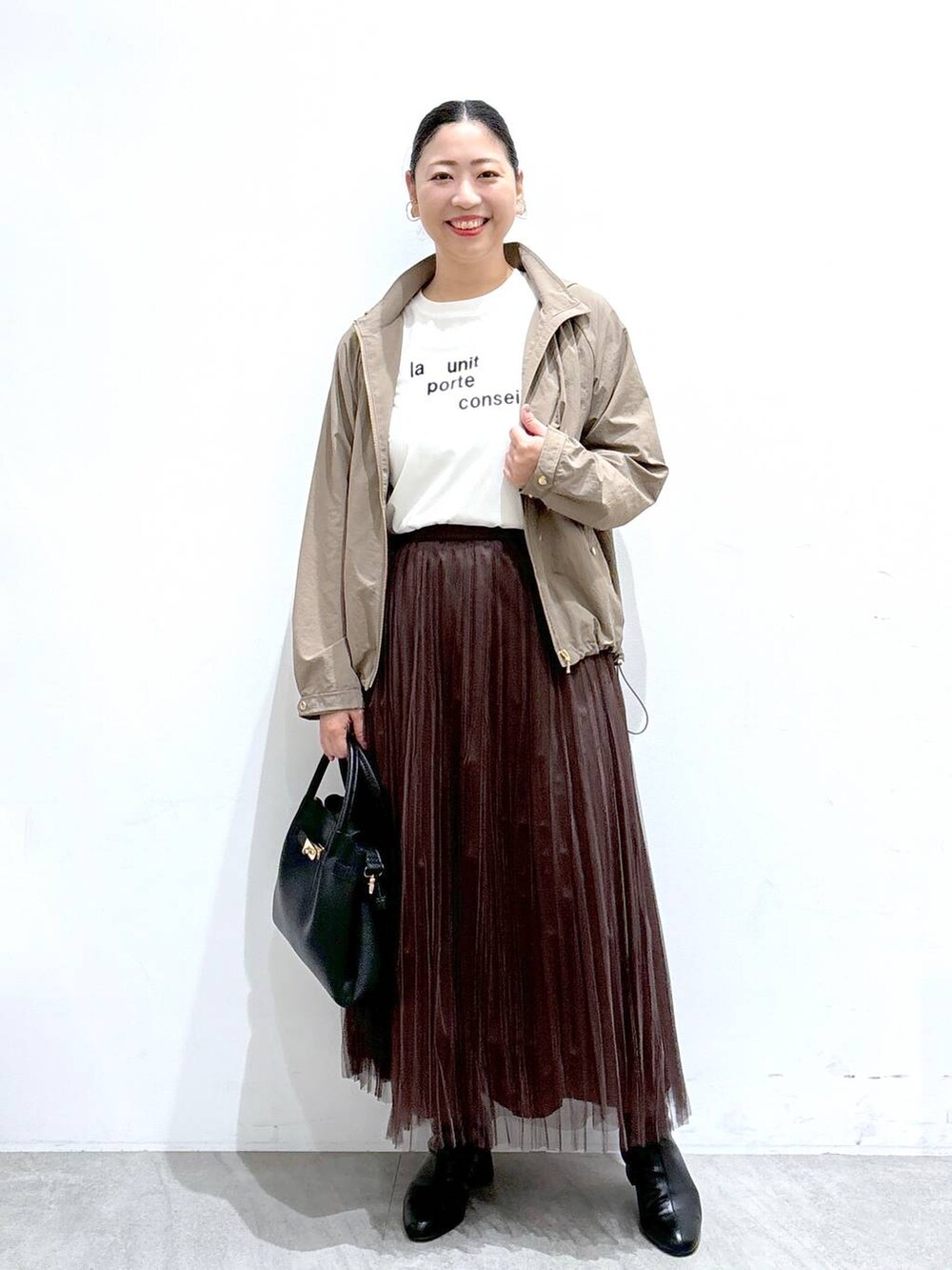 ブラック系のハンドバッグ、ブラウン系のスカート、ホワイト系のTシャツ/カットソーを着用したレディースの秋コーディネートの2枚目の写真