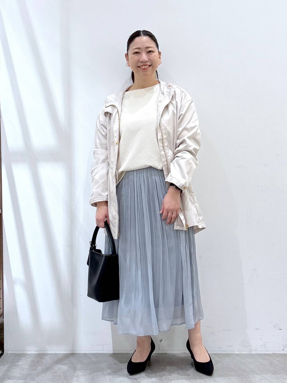 ブラック系のパンプス、ブルー系のスカート、ブラック系のハンドバッグを着用したレディースの春コーディネートの2枚目の写真