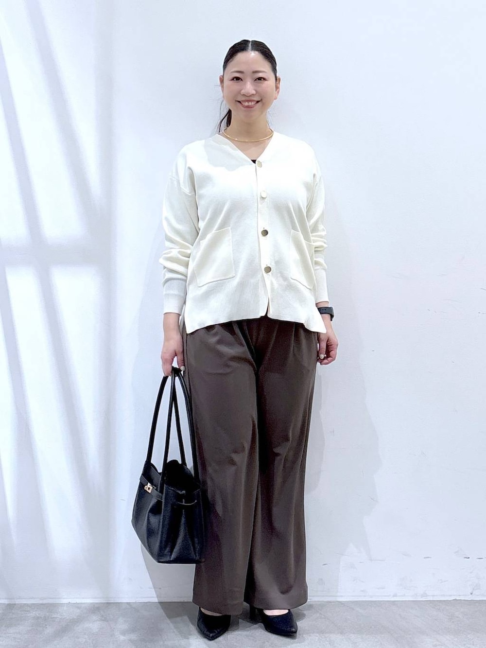 ホワイト系のカーディガン/ボレロ、ブラウン系のその他パンツ、ブラック系のハンドバッグを着用したレディースの冬コーディネートの2枚目の写真