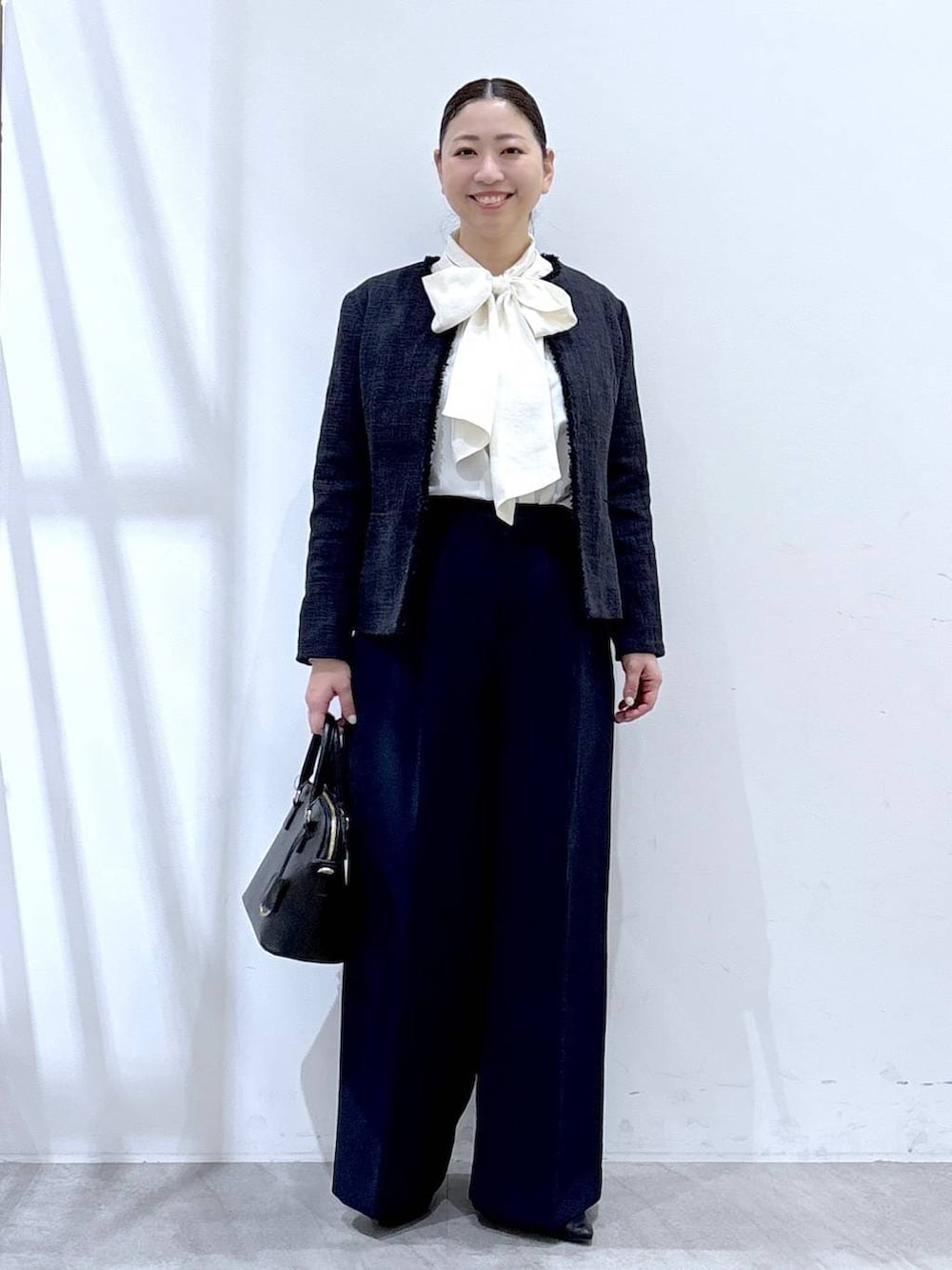 ブラック系のハンドバッグ、ブルー系のノーカラージャケット、ブルー系のスラックスを着用したレディースの冬コーディネートの2枚目の写真