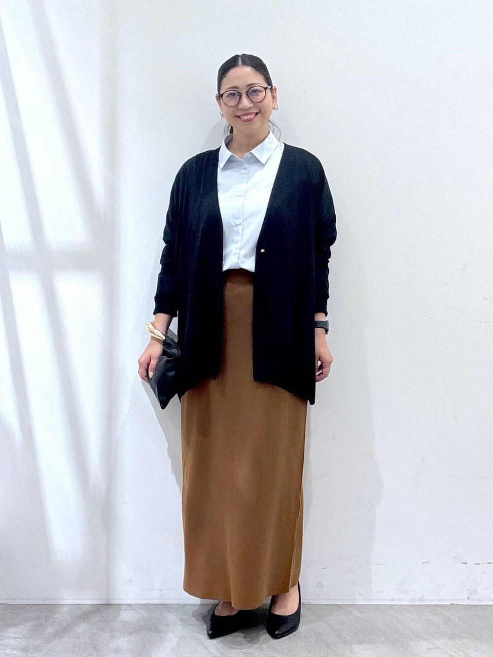 ブラック系のパンプス、ブラック系のカーディガン/ボレロ、イエロー系のスカートを着用したレディースの秋コーディネートの2枚目の写真