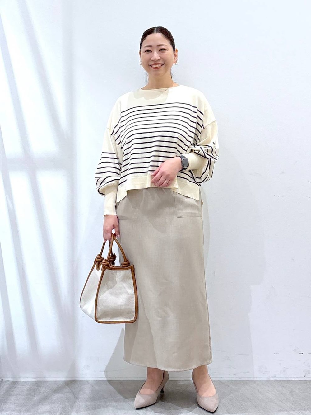 ベージュ系のパンプス、ホワイト系のスカート、ブルー系のニット/セーターを着用したレディースの春コーディネートの2枚目の写真