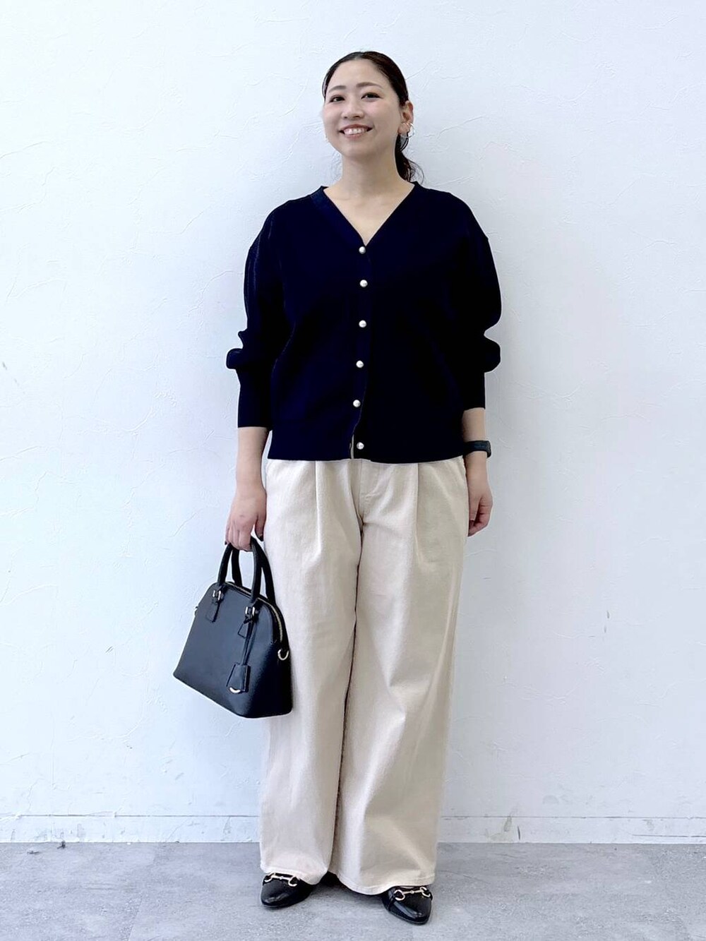 ブラック系のハンドバッグ、ベージュ系のデニムパンツ、ブラック系のパンプスを着用したレディースの冬コーディネートの2枚目の写真