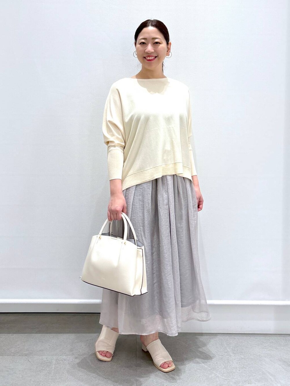 グレー系のスカート、ホワイト系のニット/セーター、ホワイト系のショルダーバッグを着用したレディースの春コーディネートの2枚目の写真