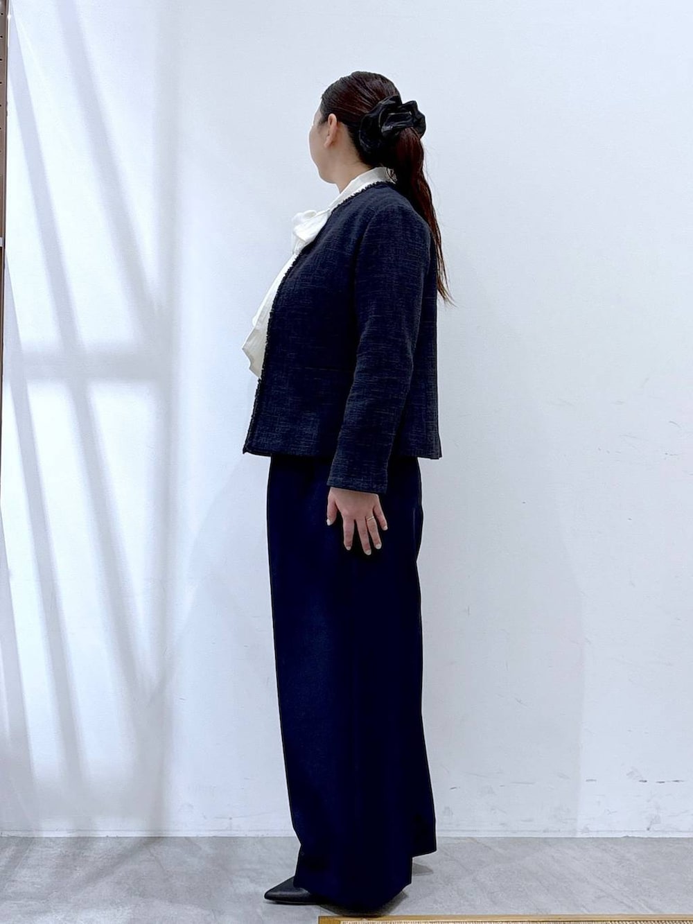 ブラック系のハンドバッグ、ブルー系のノーカラージャケット、ブルー系のスラックスを着用したレディースの冬コーディネートの3枚目の写真