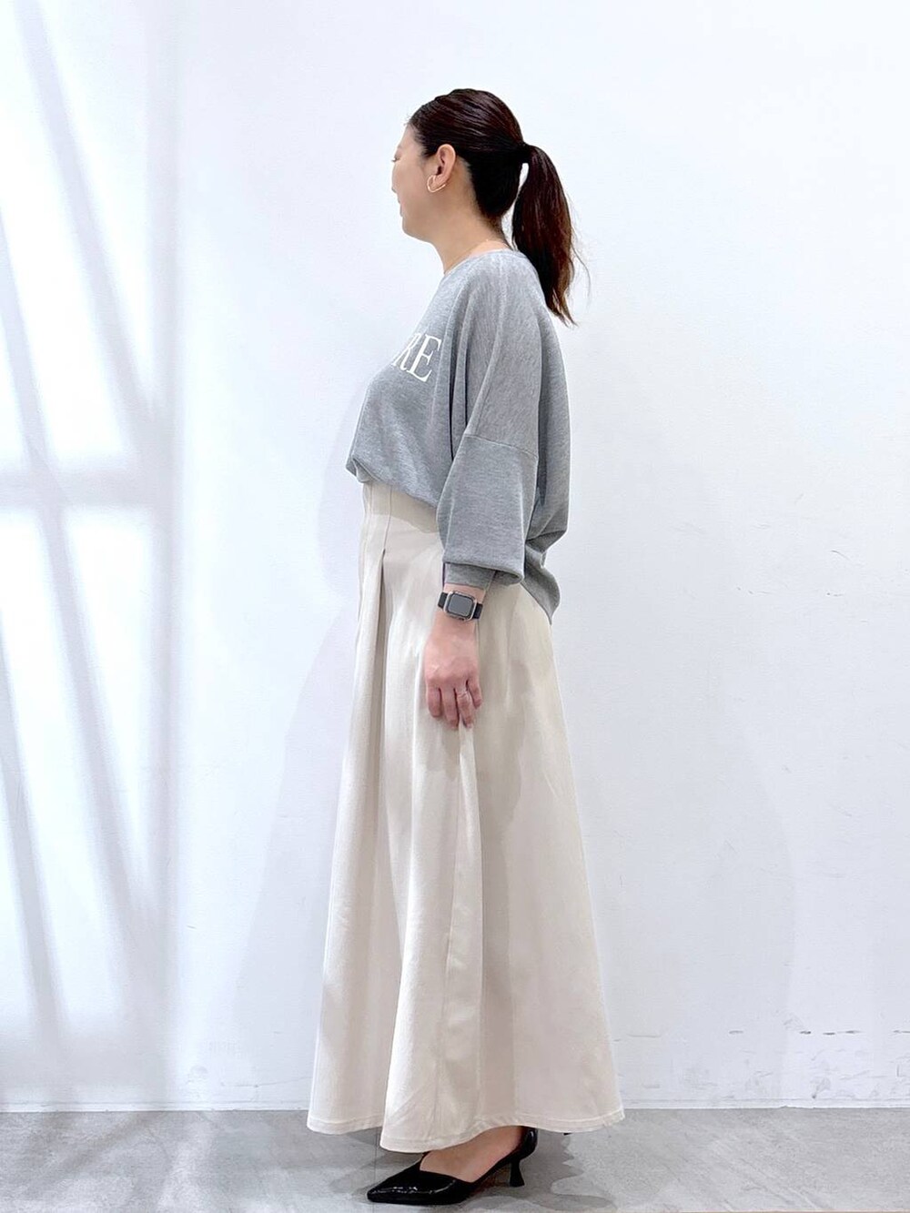 ブラック系のハンドバッグ、グレー系のニット/セーター、ベージュ系のスカートを着用したレディースの春コーディネートの3枚目の写真