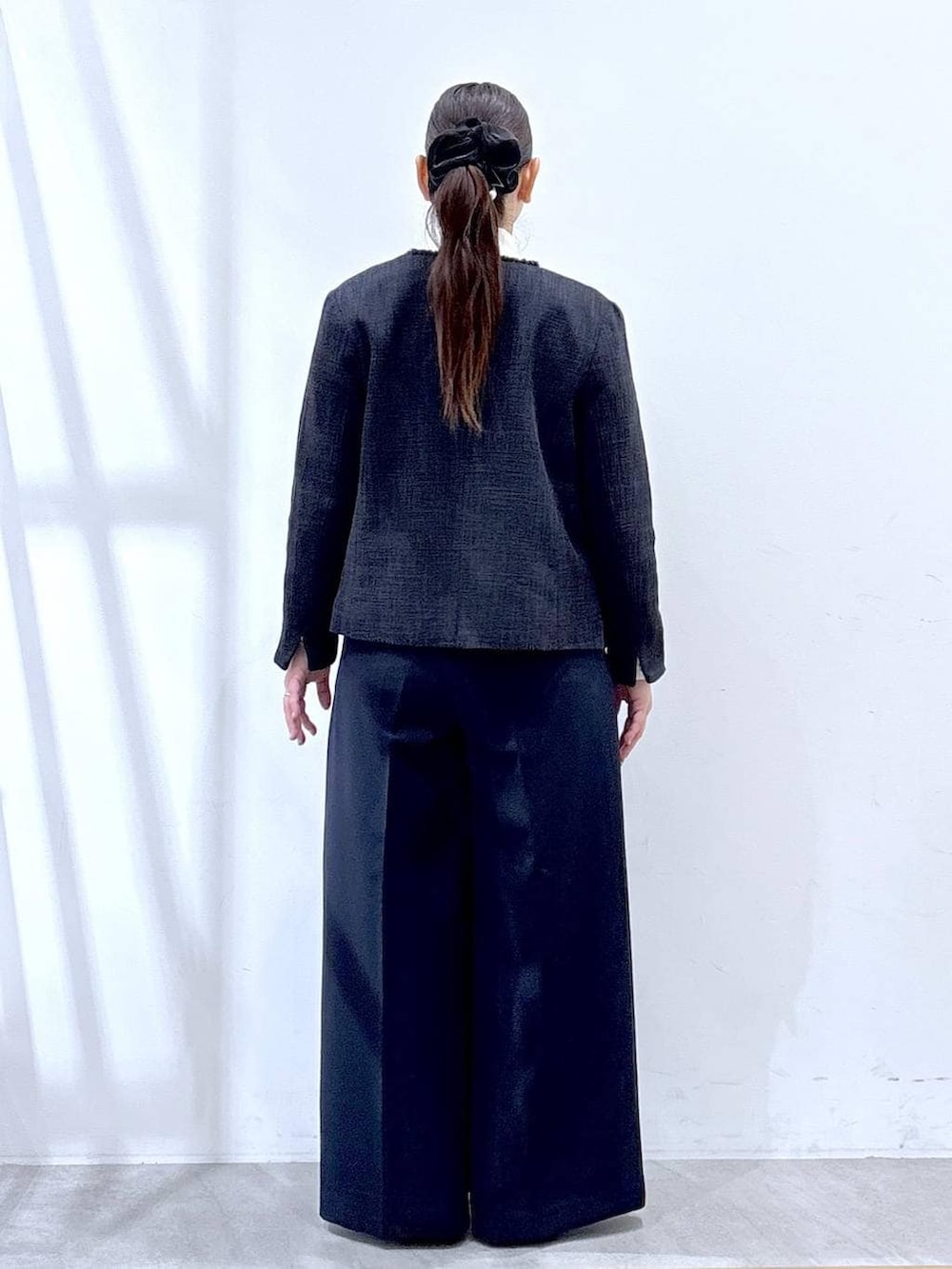 ブラック系のハンドバッグ、ブルー系のノーカラージャケット、ブルー系のスラックスを着用したレディースの冬コーディネートの4枚目の写真