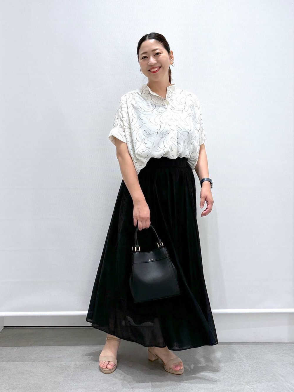 ベージュ系のサンダル、ホワイト系のシャツ/ブラウス、ブラック系のハンドバッグを着用したレディースの夏コーディネートの2枚目の写真