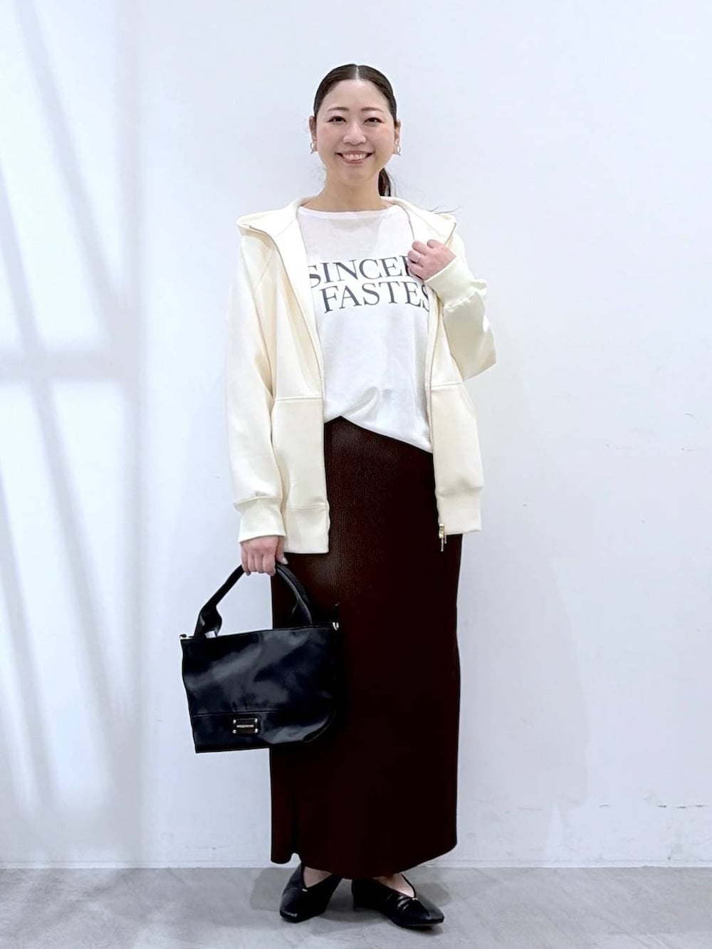ホワイト系のパーカー、ブラウン系のスカート、ブラック系のショルダーバッグを着用したレディースの春コーディネートの2枚目の写真