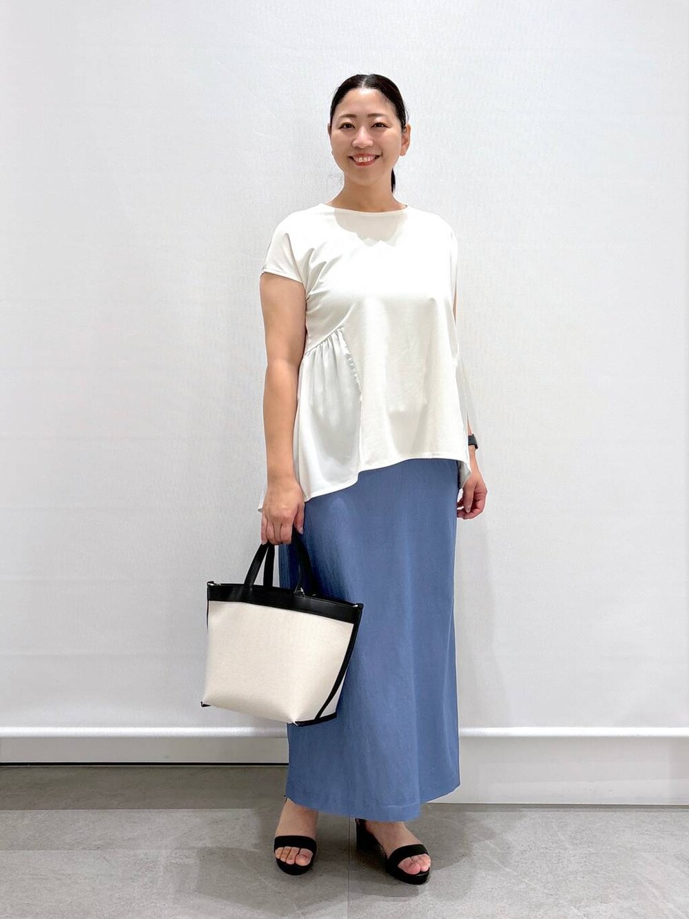 ブラック系のトートバッグ、ブラック系のサンダル、ブルー系のデニムスカートを着用したレディースの夏コーディネートの2枚目の写真