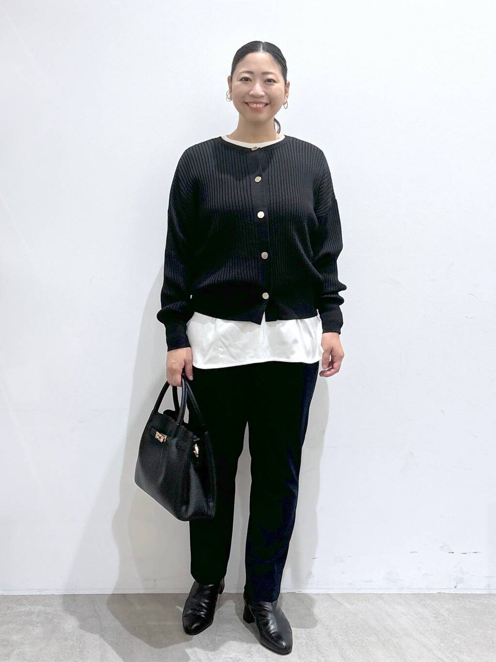 ブラック系のカーディガン/ボレロ、ブラック系のハンドバッグ、ブラック系のブーツを着用したレディースの秋コーディネートの2枚目の写真