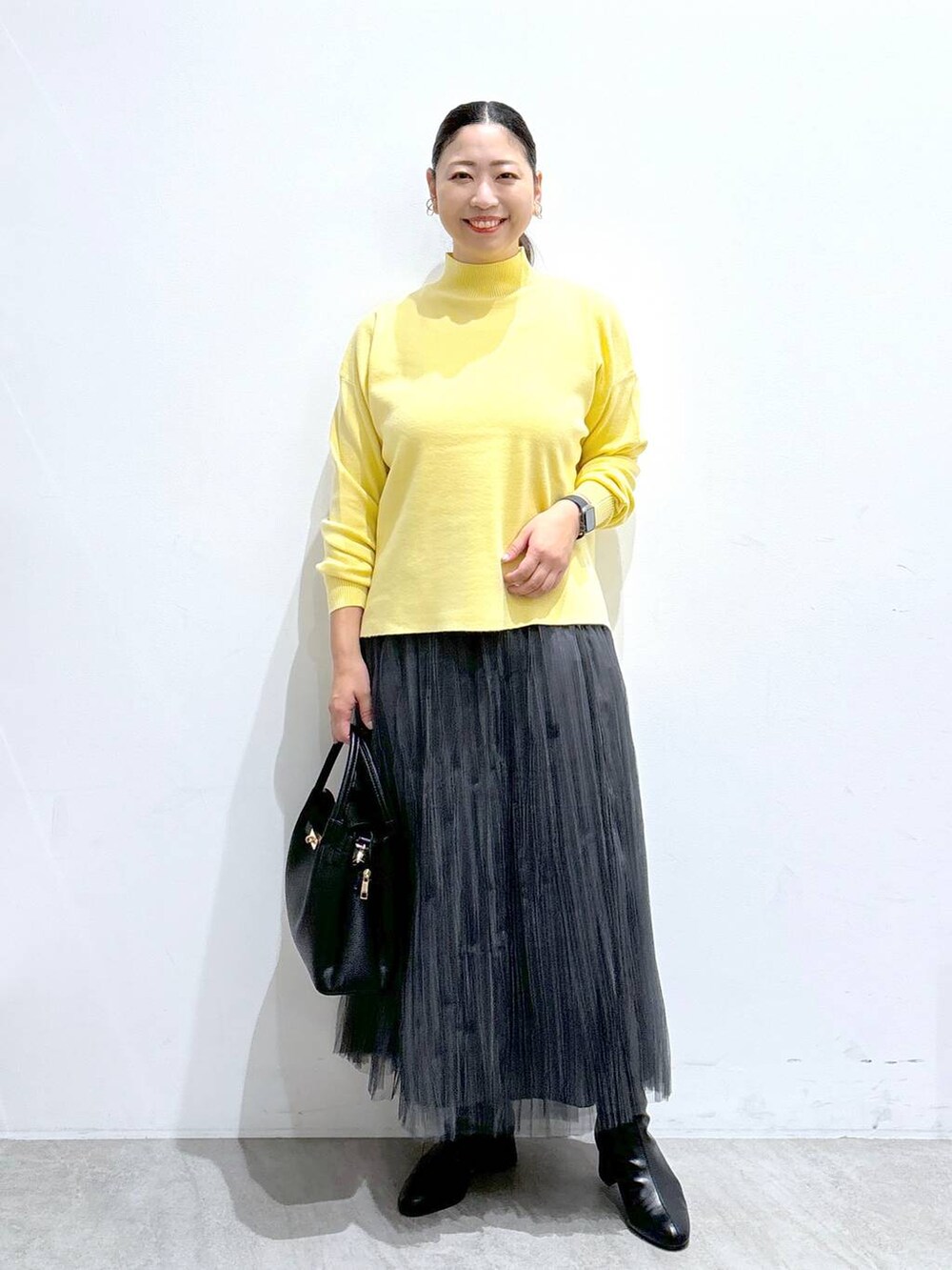 ブラック系のハンドバッグ、グレー系のスカート、ブラック系のブーツを着用したレディースの秋コーディネートの2枚目の写真