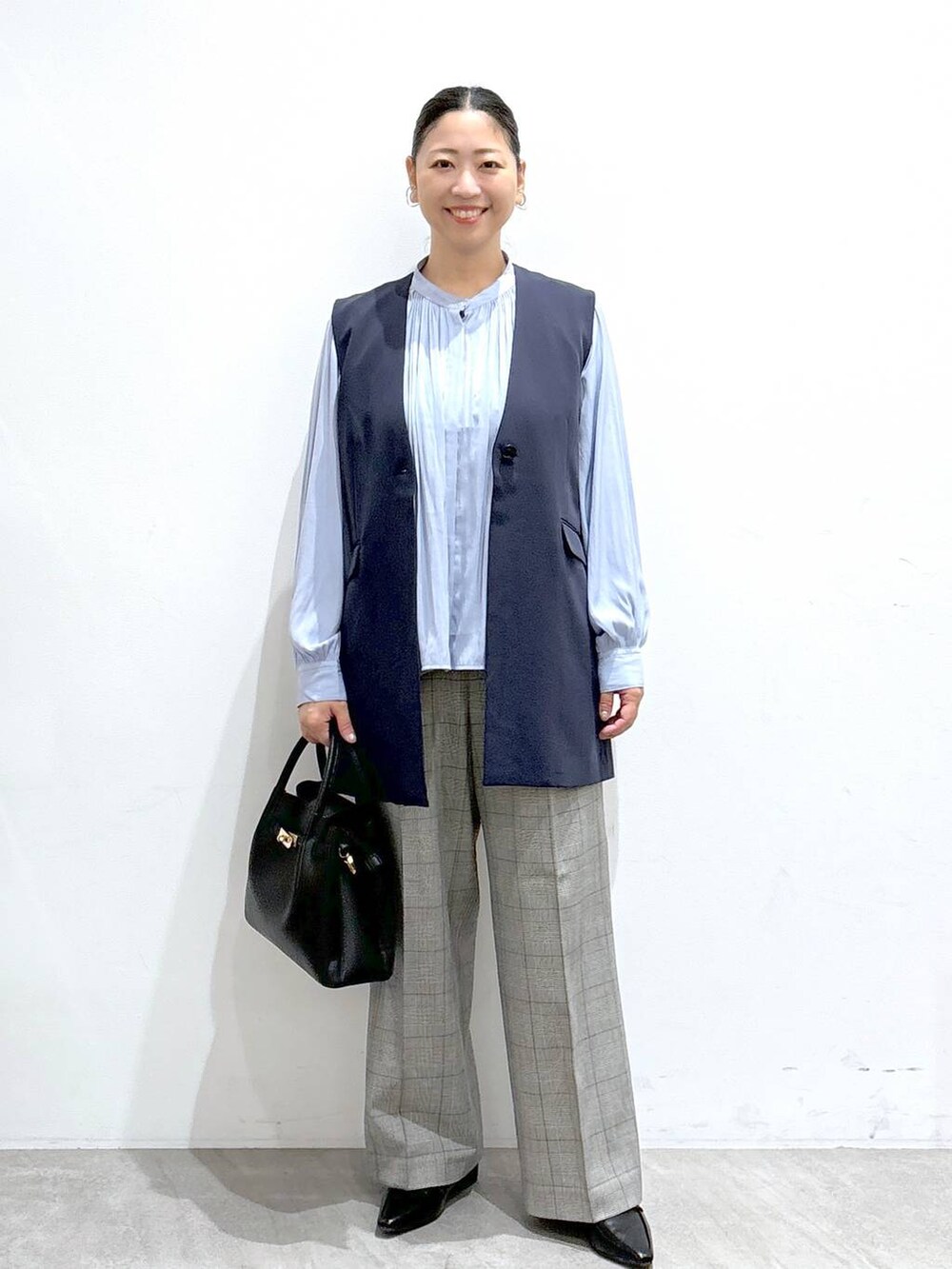 ブルー系のベスト、ブラック系のハンドバッグ、ブルー系のシャツ/ブラウスを着用したレディースの秋コーディネートの2枚目の写真