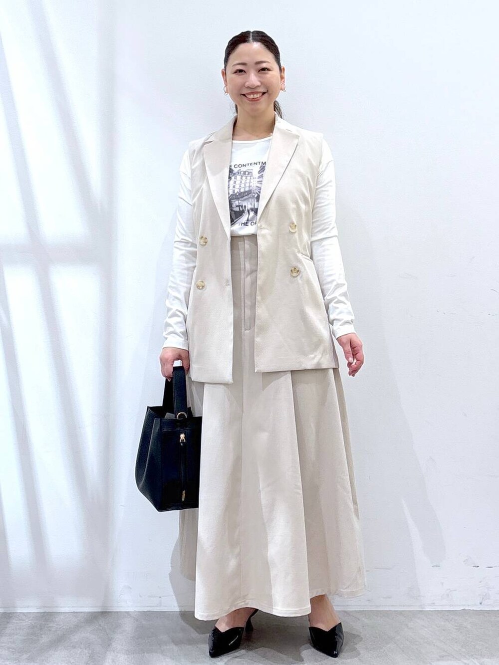 ベージュ系のスカート、ベージュ系のベスト、ホワイト系のTシャツ/カットソーを着用したレディースの春コーディネートの2枚目の写真