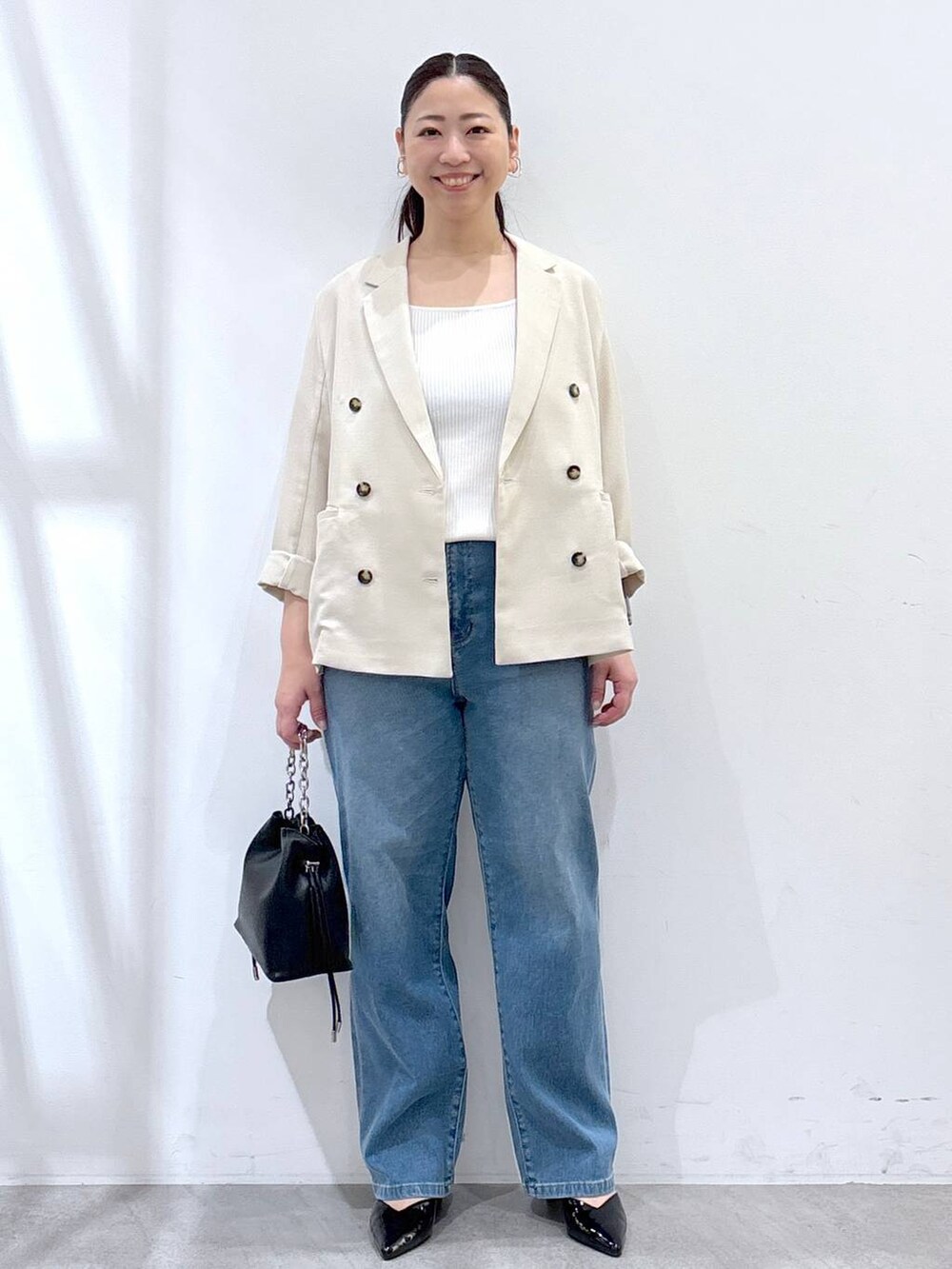 ブルー系のデニムパンツ、ベージュ系のテーラードジャケット、ホワイト系のタンクトップを着用したレディースの春コーディネートの2枚目の写真
