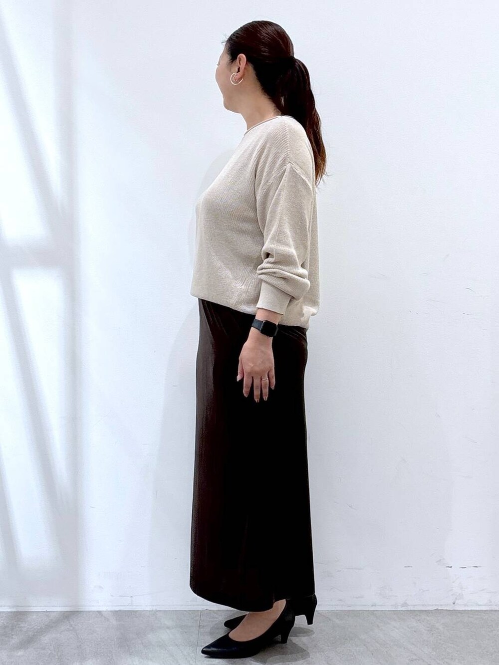 ブラック系のパンプス、ブラック系のハンドバッグ、ブラウン系のスカートを着用したレディースの秋コーディネートの3枚目の写真