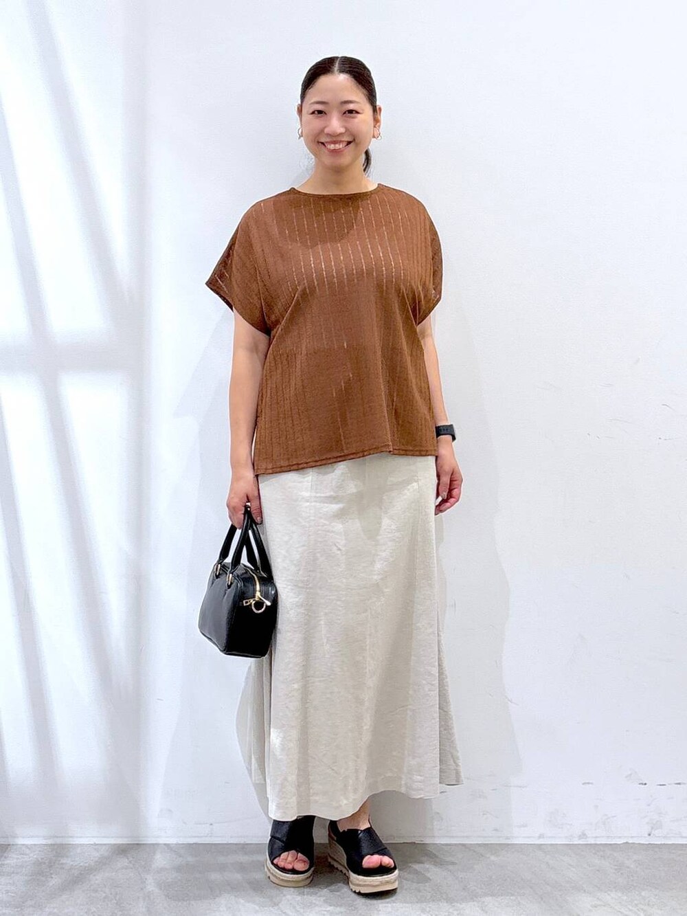 ベージュ系のスカート、ブラック系のハンドバッグ、ブラウン系のTシャツ/カットソーを着用したレディースの夏コーディネートの2枚目の写真
