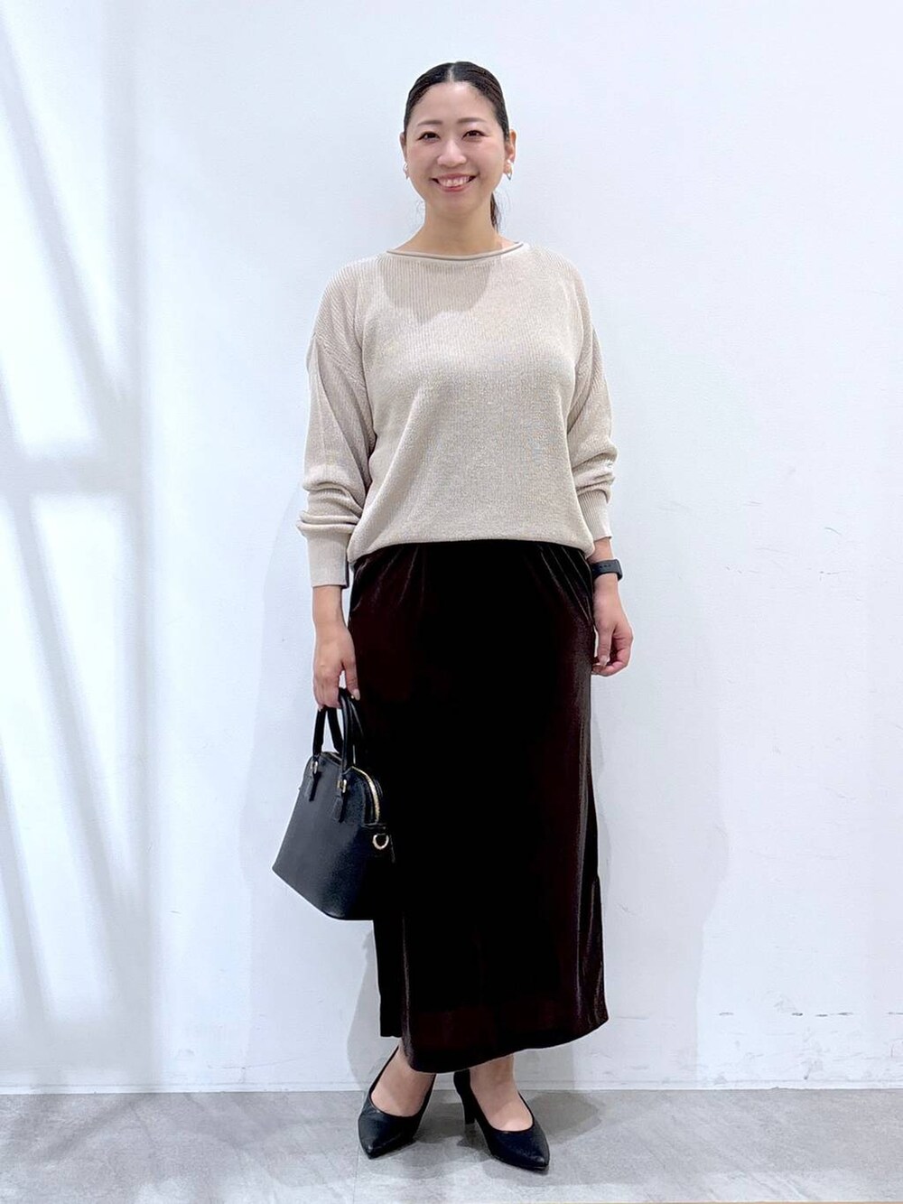 ブラック系のパンプス、ブラック系のハンドバッグ、ブラウン系のスカートを着用したレディースの秋コーディネートの2枚目の写真