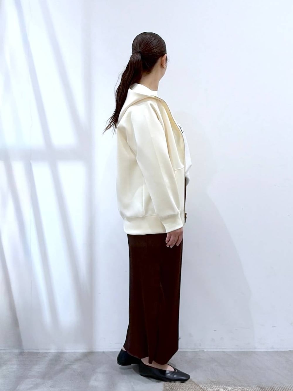ホワイト系のパーカー、ブラウン系のスカート、ブラック系のショルダーバッグを着用したレディースの春コーディネートの5枚目の写真