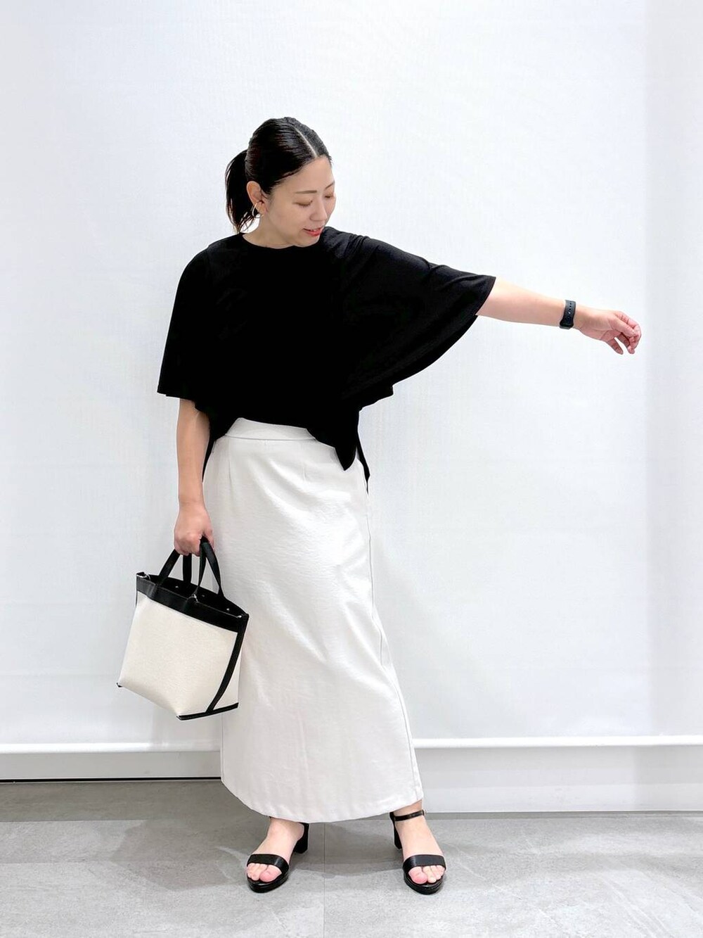 ブラック系のトートバッグ、グレー系のスカート、ブラック系のサンダルを着用したレディースの夏コーディネートの2枚目の写真