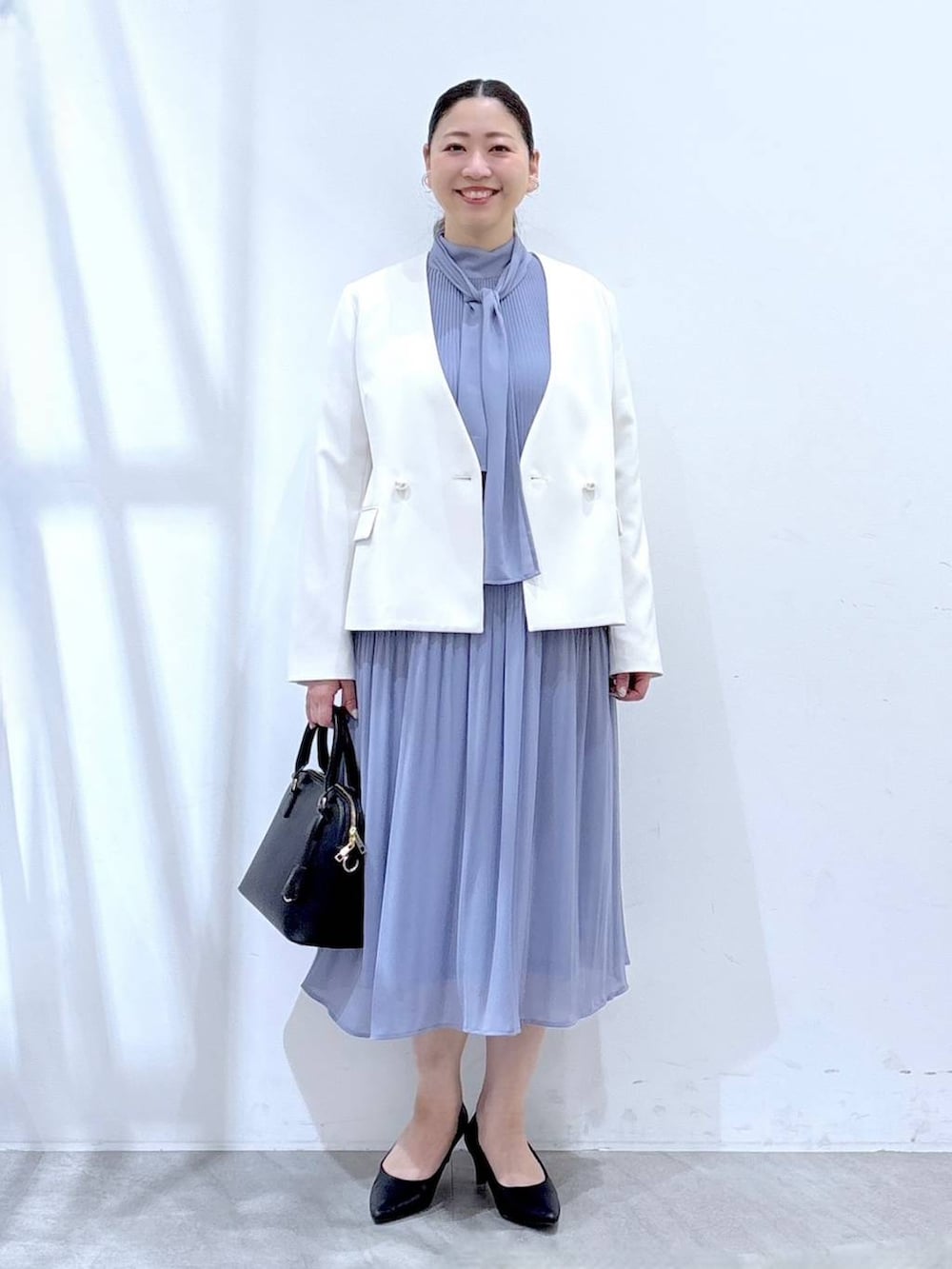 ブラック系のハンドバッグ、ホワイト系のノーカラージャケット、ブルー系のワンピースを着用したレディースの冬コーディネートの2枚目の写真