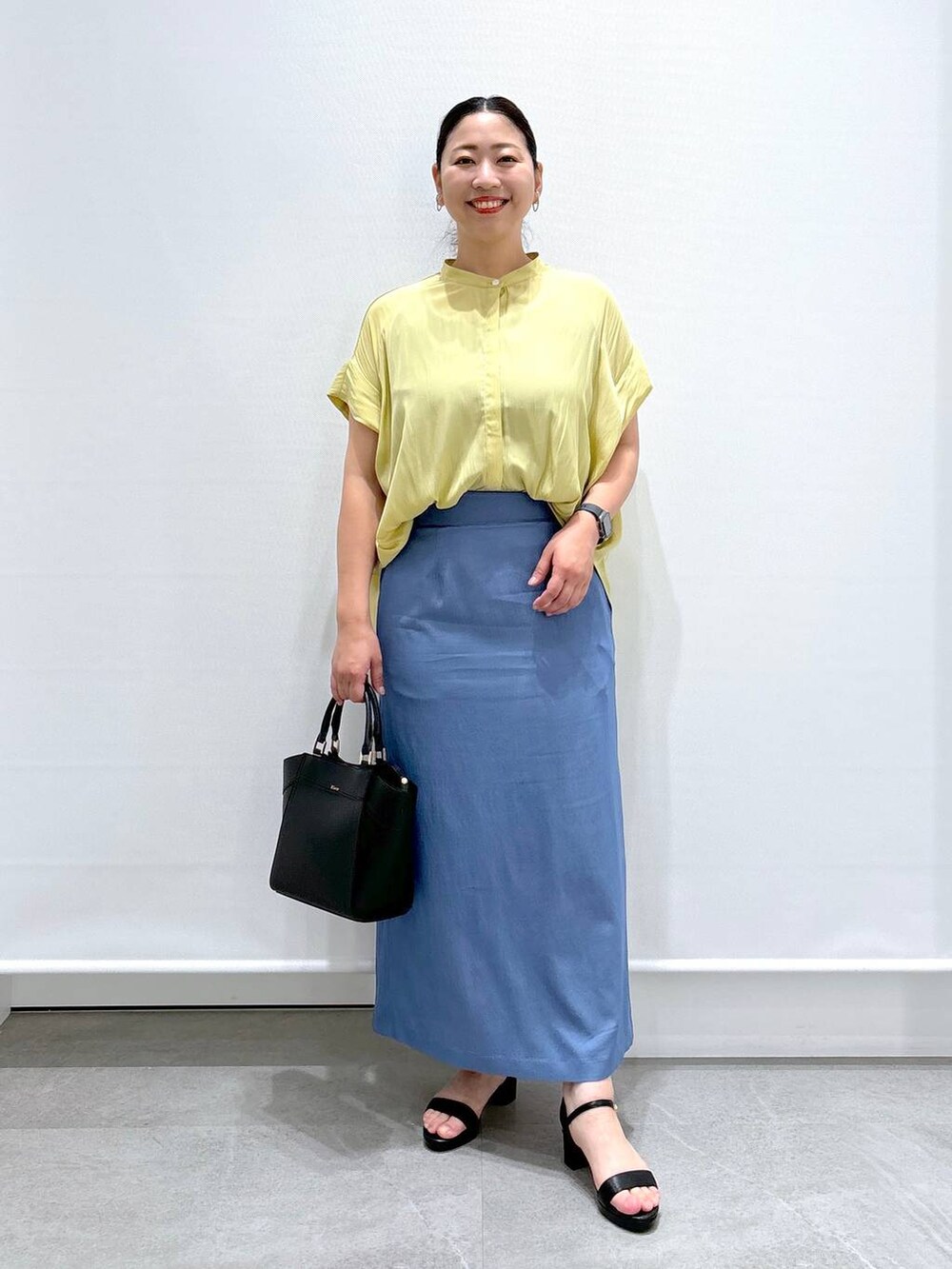 イエロー系のシャツ/ブラウス、ブラック系のサンダル、ブラック系のハンドバッグを着用したレディースの夏コーディネートの2枚目の写真