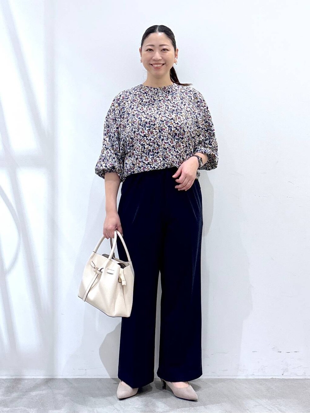 ベージュ系のパンプス、ベージュ系のハンドバッグ、ブルー系のノーカラージャケットを着用したレディースの春コーディネートの2枚目の写真