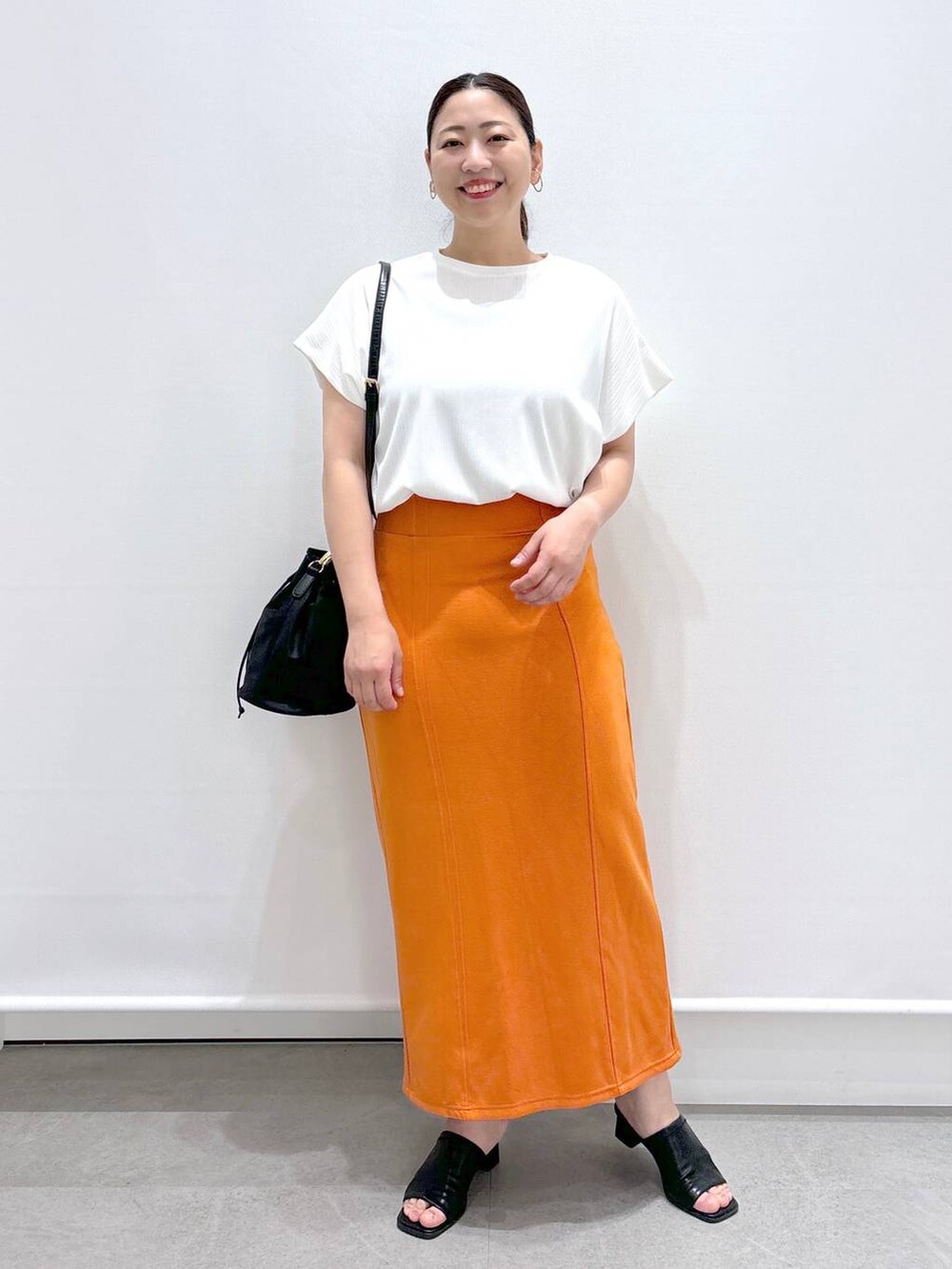 ブラック系のサンダル、ホワイト系のTシャツ/カットソー、オレンジ系のスカートを着用したレディースの春コーディネートの2枚目の写真